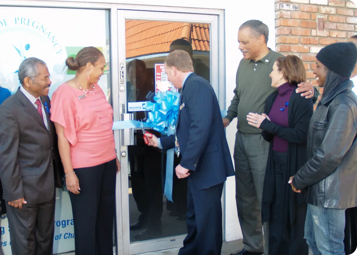 A group cutting a ribbon at the door of a Claris clinic