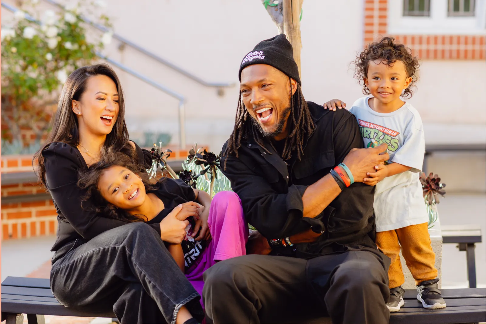 A laughing family of four sitting together on a bench